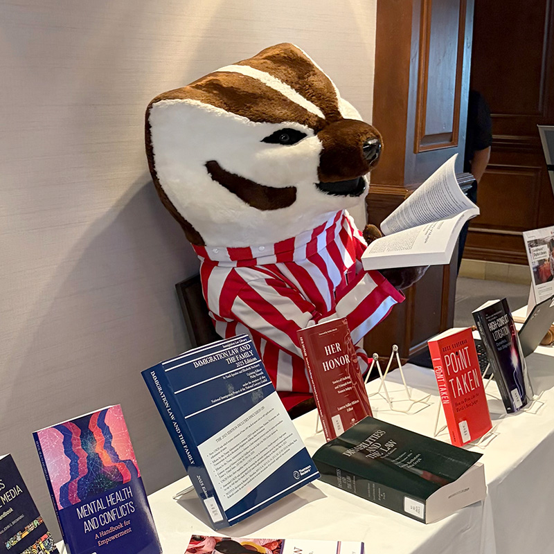 Bucky Badger mascot reclining in a chair and reading law books at a table